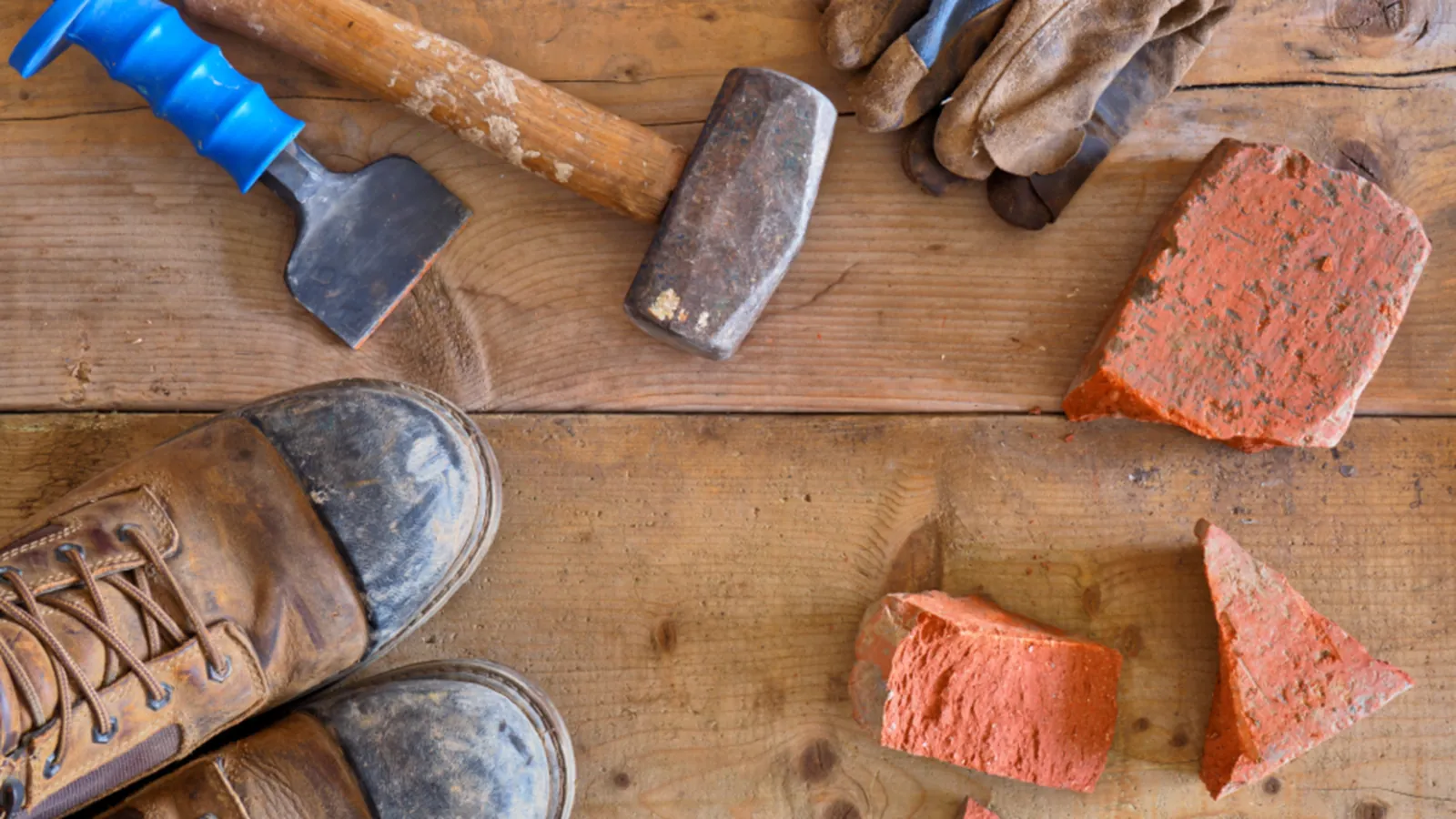 Hammer, Ziegelbruchstücke, Arbeitshandschuhe und Arbeitsschuhe auf Holzbrettern