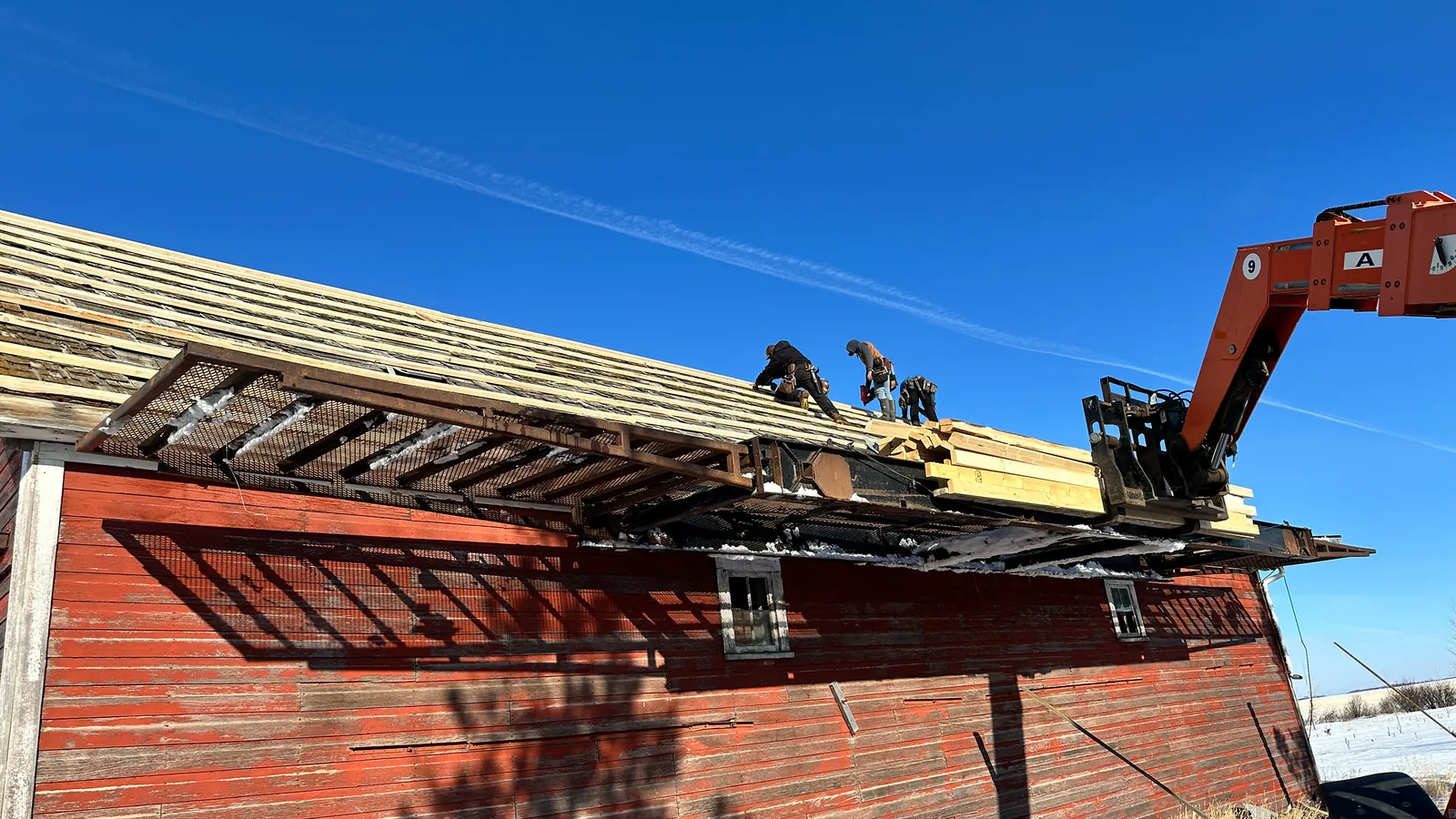 Dachdecker arbeiten mit Kran am Dachstuhl eines roten Holzgebäudes