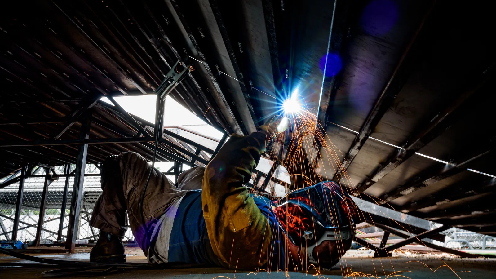 Schweißer liegt unter einer Metallkonstruktion, Funken sprühen