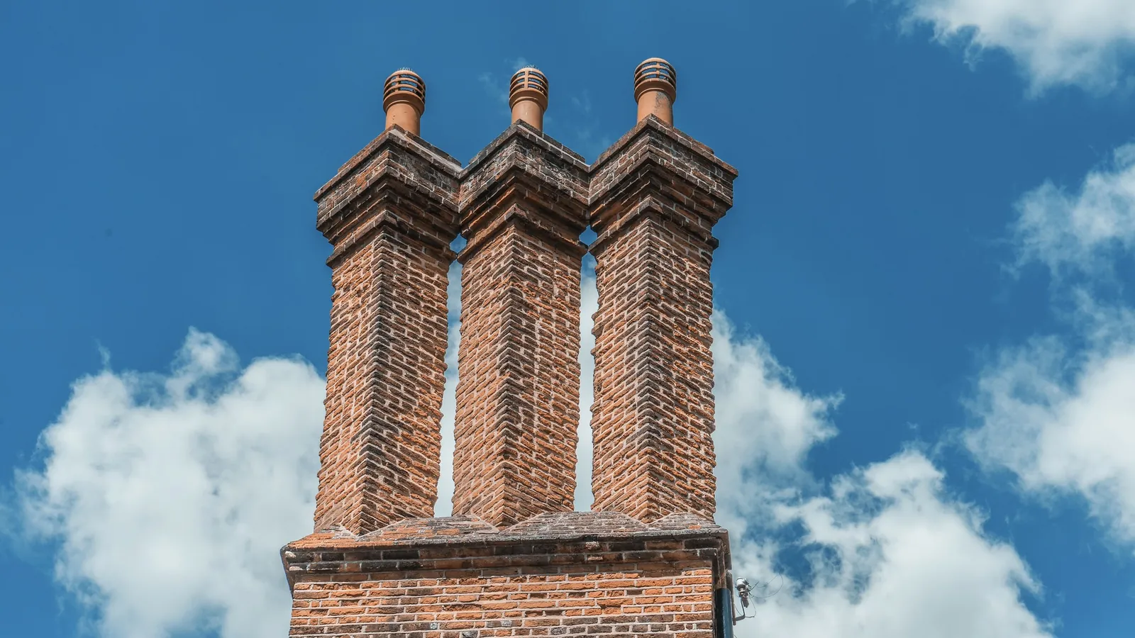 Drei gemauerte Schornsteine aus Backstein vor blauem Himmel