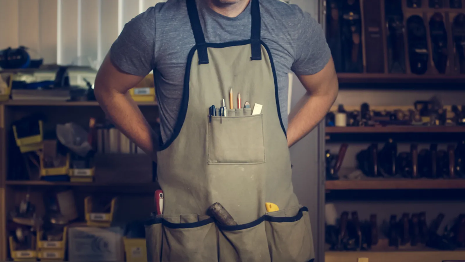 Handwerker in Schürze steht mit Werkzeugen im Regal in einer Werkstatt