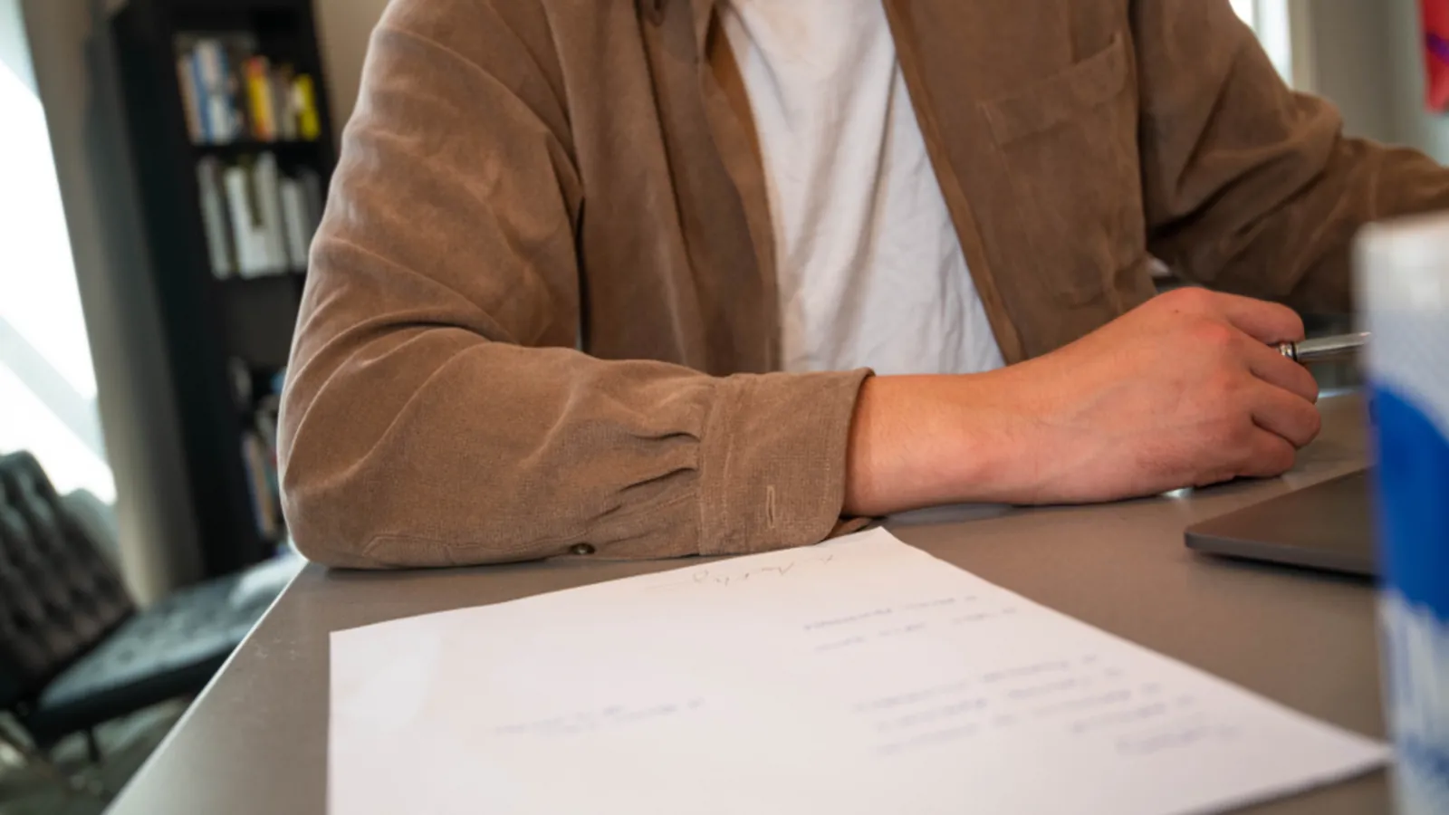 Person sitzt an einem Schreibtisch mit Papierdokument und Stift