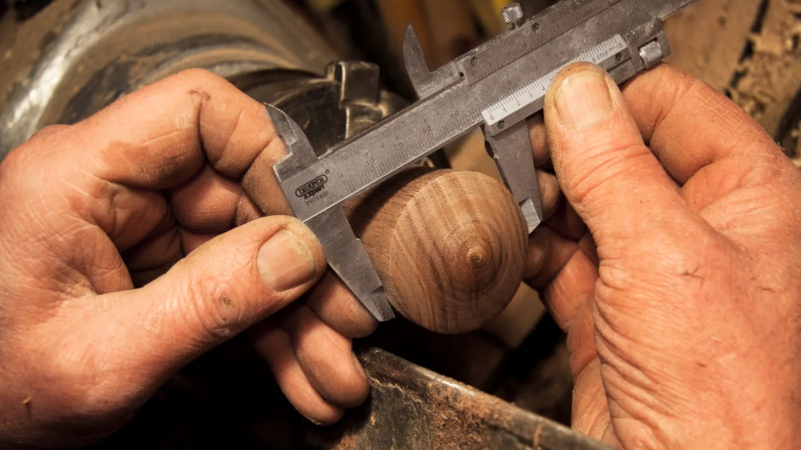 Hände messen ein gedrechseltes Holzstück mit einem Messschieber